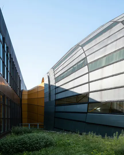Un moderno complesso architettonico con un edificio scuro con finestre rettangolari, una struttura curva arancione e una