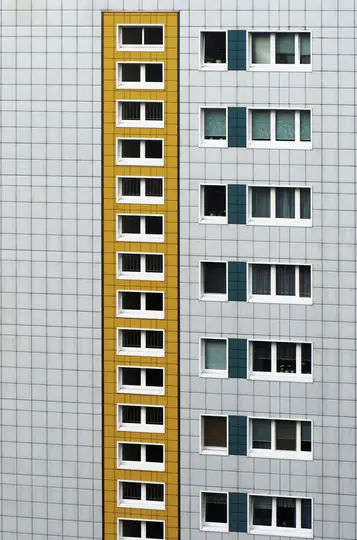 Una vista ravvicinata, a schermo intero, della facciata di un edificio moderno, con una prominente striscia verticale gialla.
