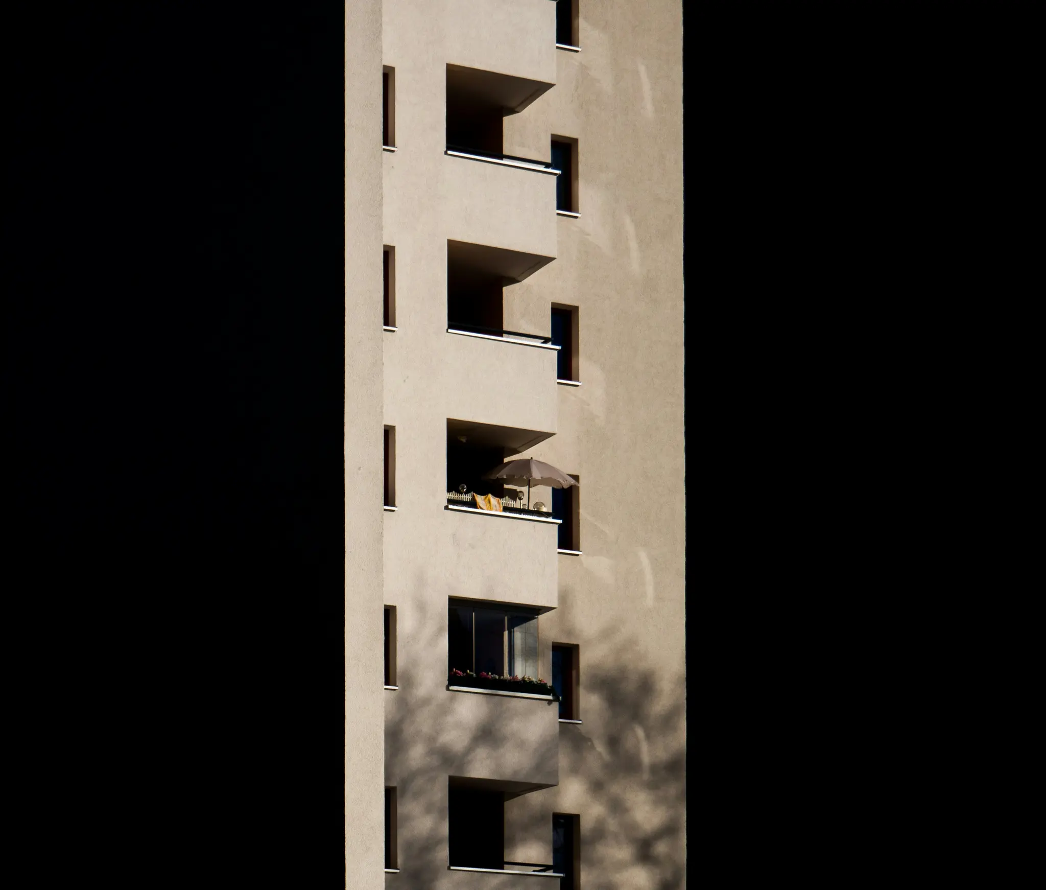 Béžová moderná fasáda budovy s viacerými balkónmi a oknami. Slnečné svetlo osvetľuje časti budovy a vrhá…
