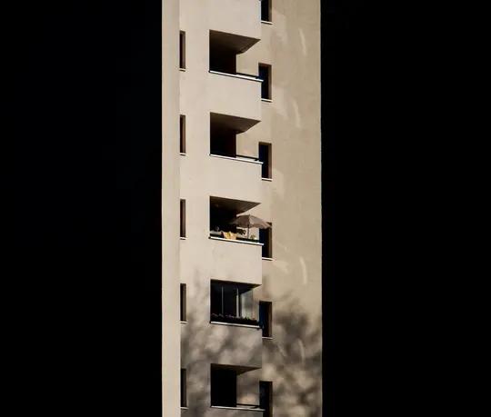 Una facciata di edificio moderna e beige con numerosi balconi e finestre. La luce del sole illumina parti dell'edificio