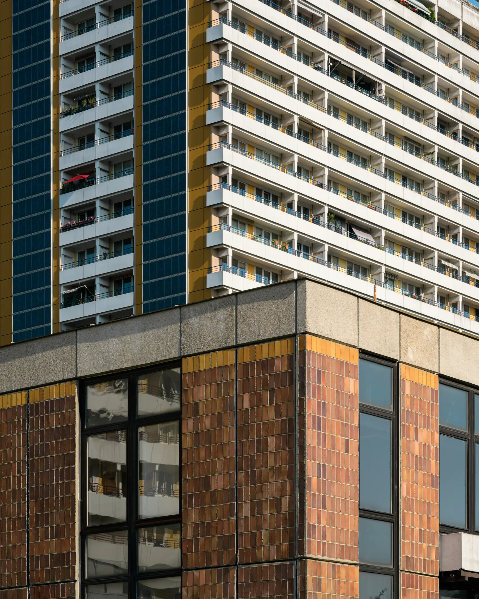 Una vista detallada de dos fachadas de edificios. Uno es un rascacielos alto, amarillo y azul con balcones blancos. El otro