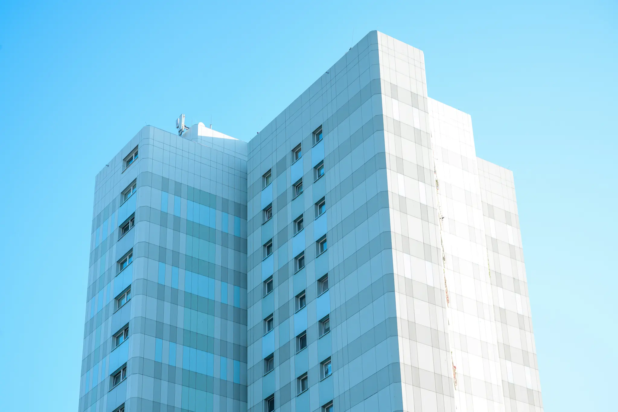 Una toma de ángulo bajo de un edificio alto y moderno con una fachada de paneles azul claro, gris y blanco, contra un cielo