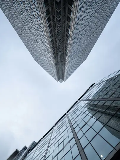 Una vista dal basso di due moderni grattacieli con facciate in vetro e acciaio, uno che punta verso l'alto dall'alto e
