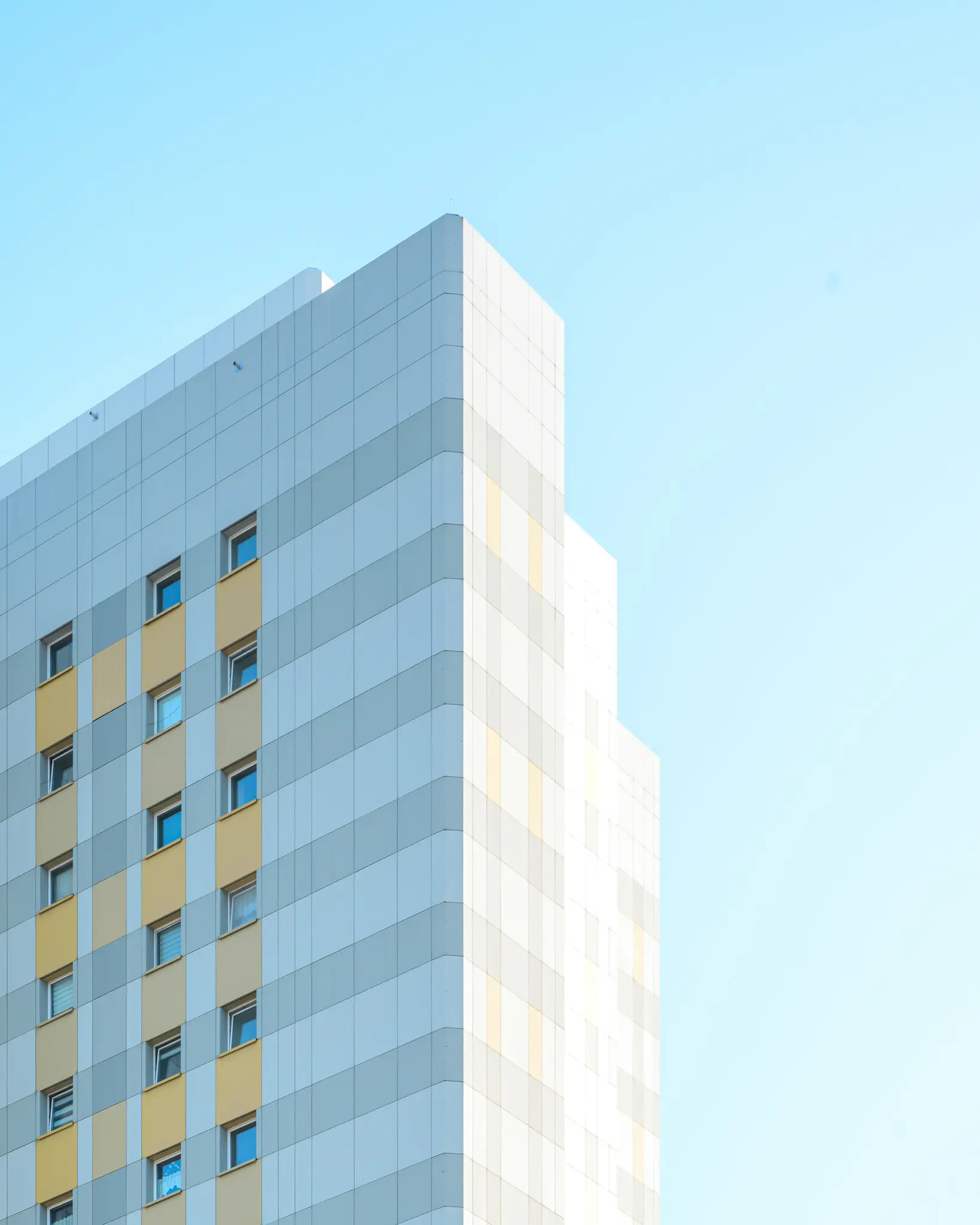 Una toma desde un ángulo bajo de un edificio moderno con una fachada de paneles gris claro, blancos y amarillo pálido, contra
