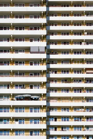 Un alto edificio residenziale con facciata gialla e balconi bianchi con ringhiere rosso scuro. Molte finestre riflettono il