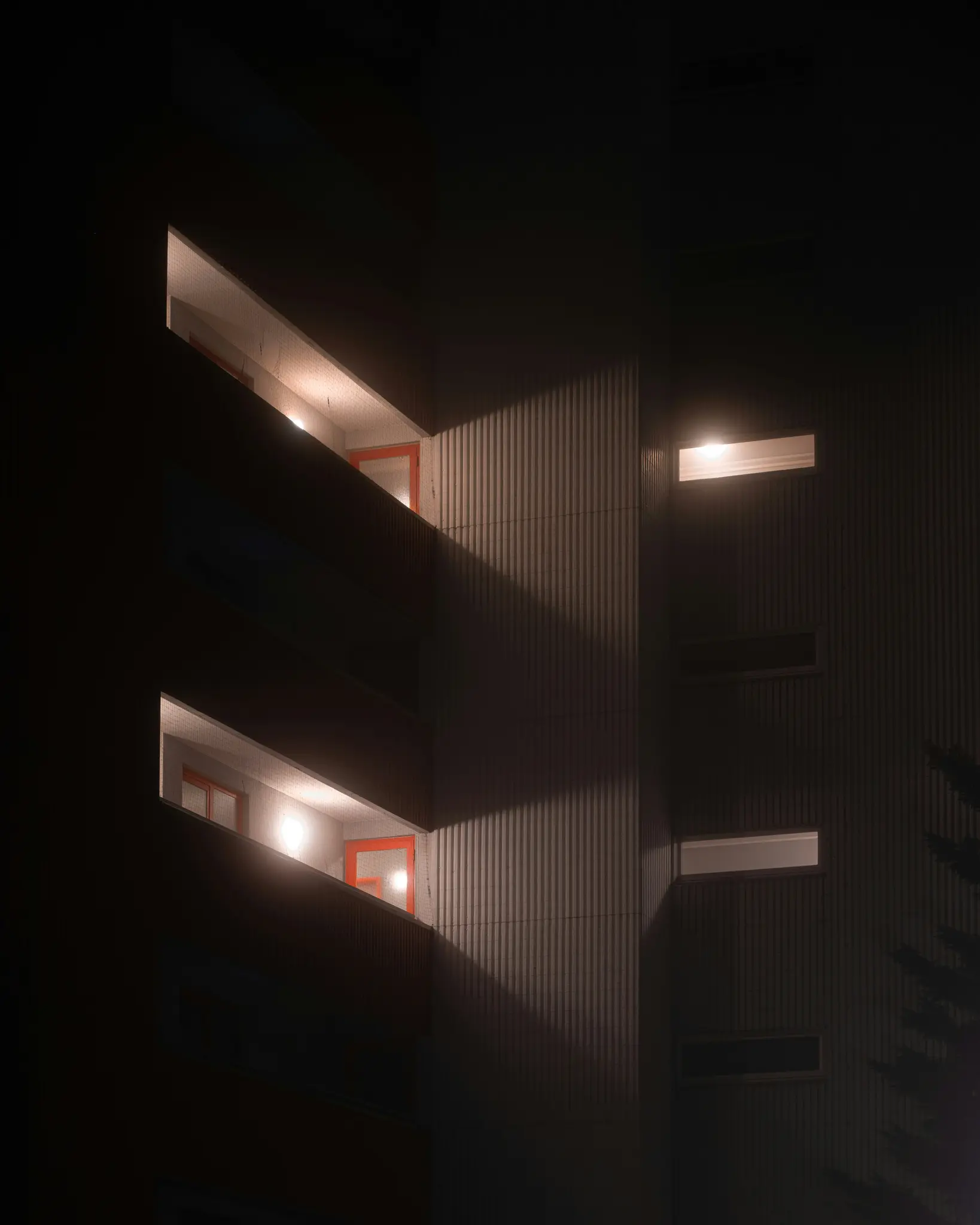 Un plano oscuro y vertical de la fachada de un edificio por la noche. Varias ventanas están brillantemente iluminadas