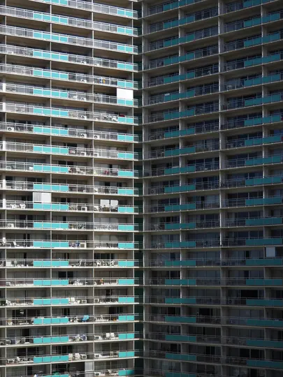 Una vista ravvicinata, a schermo intero, di due alti condomini. Gli edifici sono grigi con balconi bianchi e ringhiere