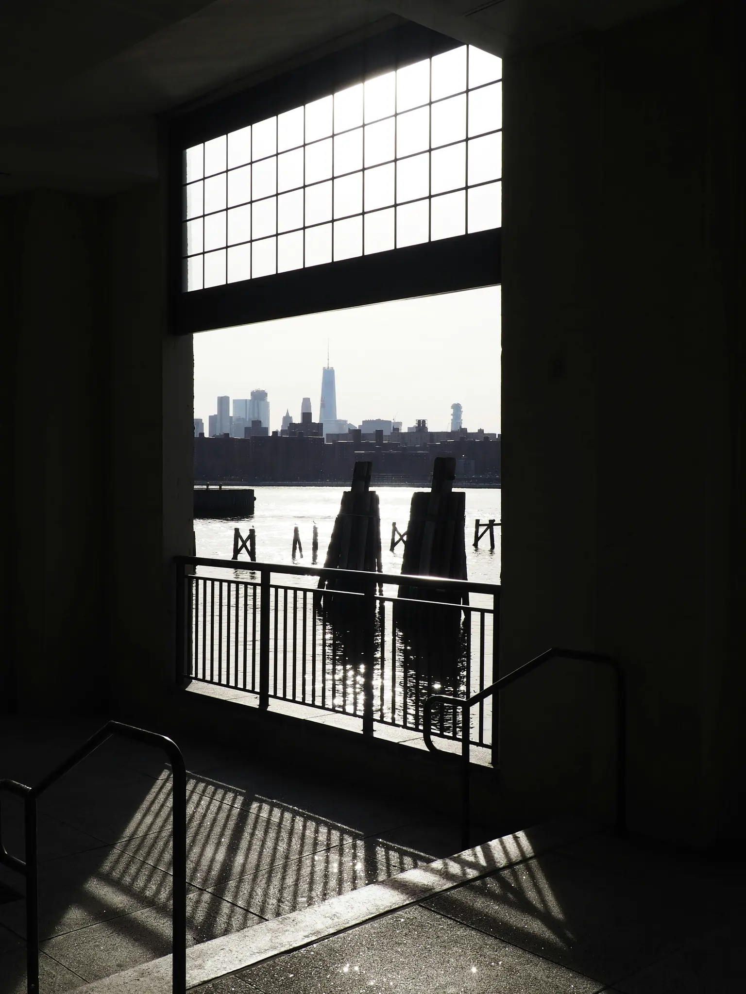Una foto de alto contraste que muestra un horizonte urbano sobre el agua, visto a través de una gran ventana cuadriculada