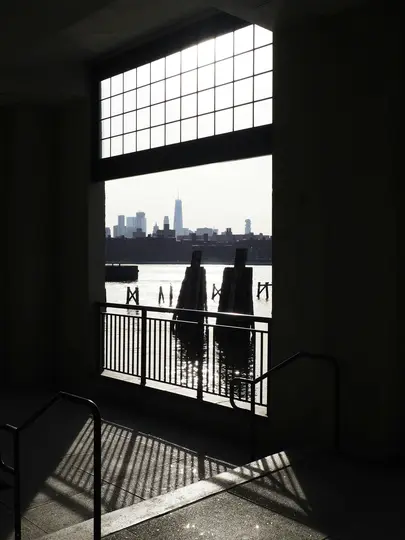 Una foto ad alto contrasto che mostra uno skyline cittadino sull'acqua, visto attraverso una grande finestra a griglia da un