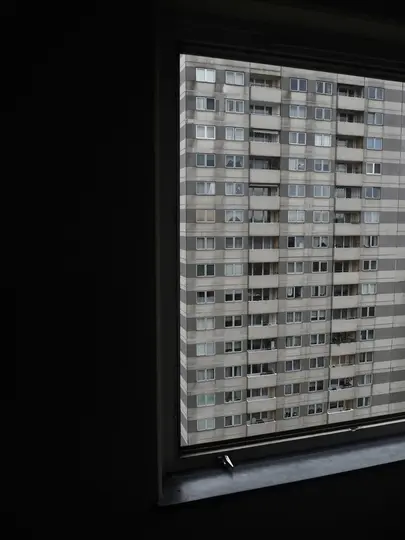 Una vista austera de un edificio residencial alto y gris con numerosas ventanas y balcones, vista a través de un marco de