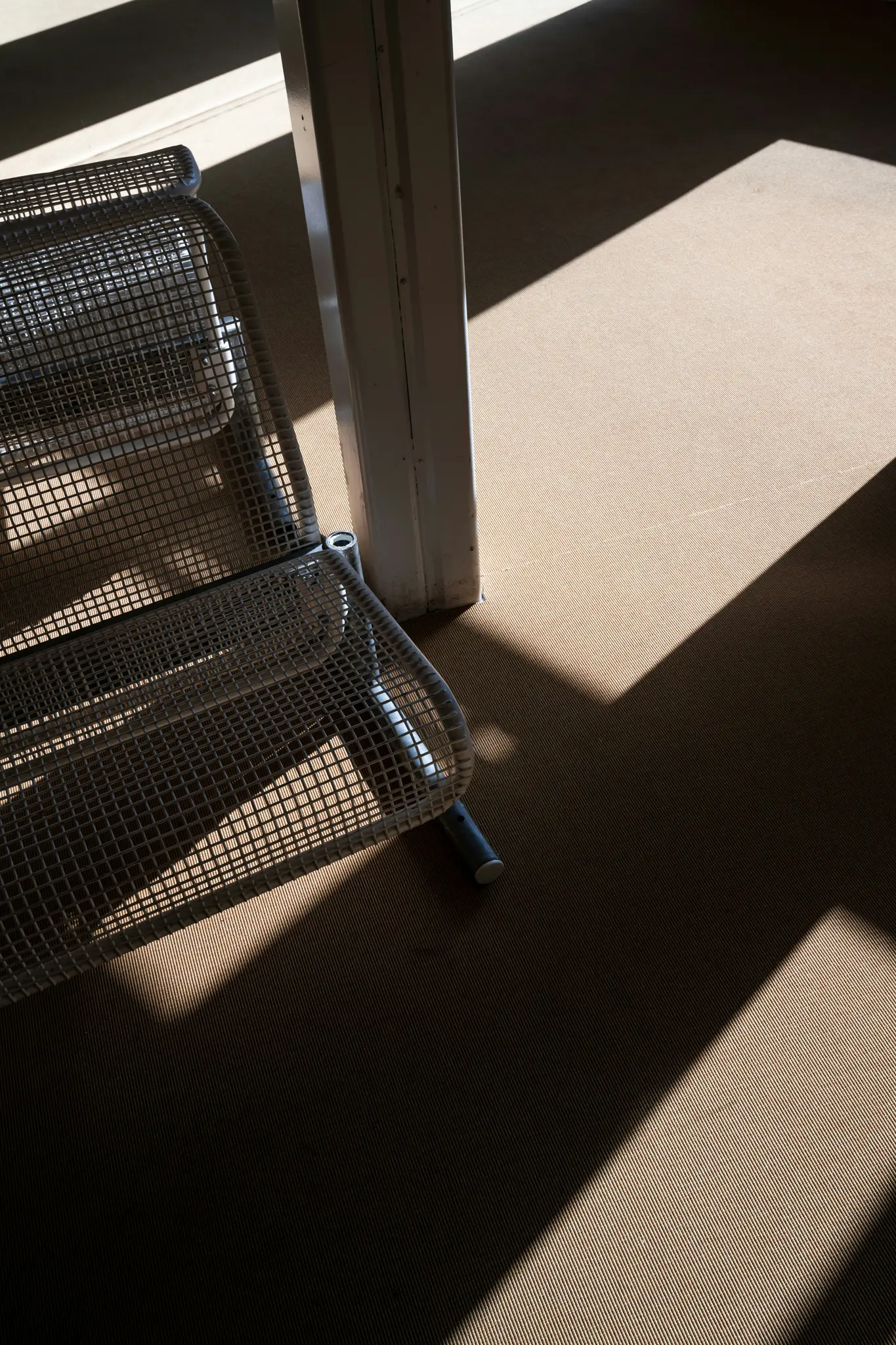 Un primer plano de una silla de malla metálica que proyecta intrincadas sombras sobre un suelo texturizado de color marrón