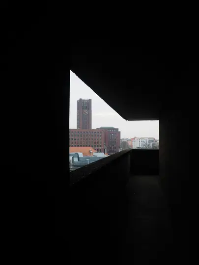 Ein städtisches Gebäude mit einem markanten Glockenturm ist durch eine dunkle, eckige architektonische Öffnung sichtbar. Der