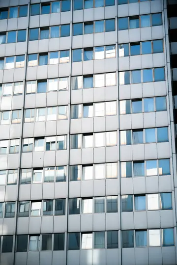Eine Nahaufnahme aus niedriger Perspektive der Fassade eines hohen Gebäudes mit zahlreichen rechteckigen Fenstern, die den