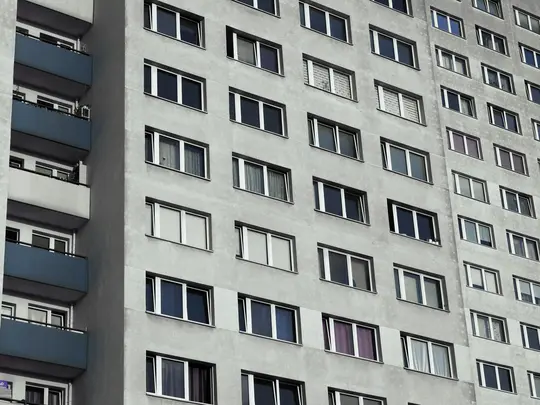 Una vista ravvicinata, leggermente angolata, della facciata di un alto condominio grigio con molte finestre rettangolari e