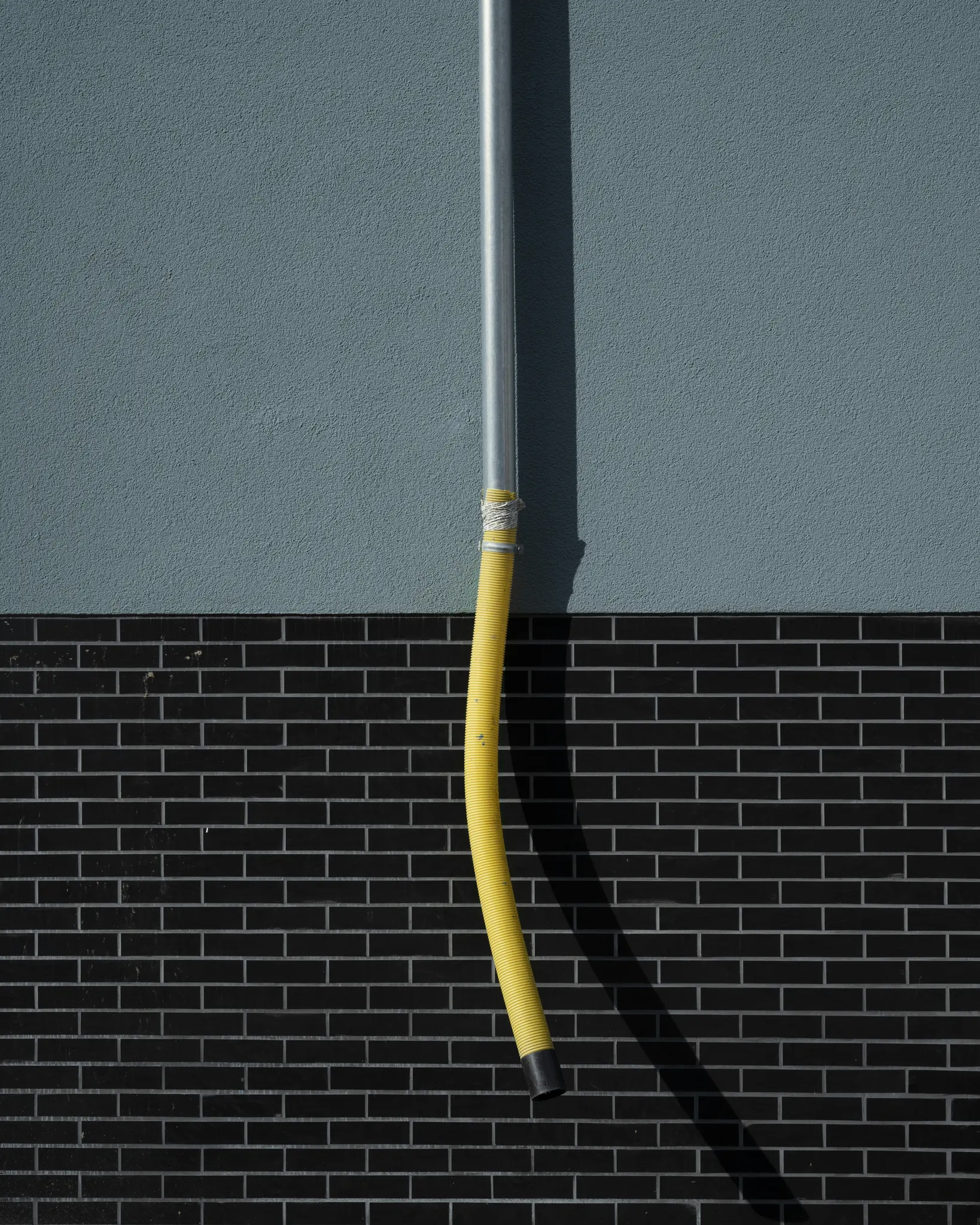 Un tubo corrugado amarillo brillante cuelga de un tubo plateado contra una pared. La pared es azul grisáceo en la parte