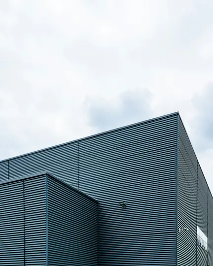 Uno scatto minimalista dell'angolo di un edificio moderno con rivestimento metallico ondulato grigio scuro sotto un cielo