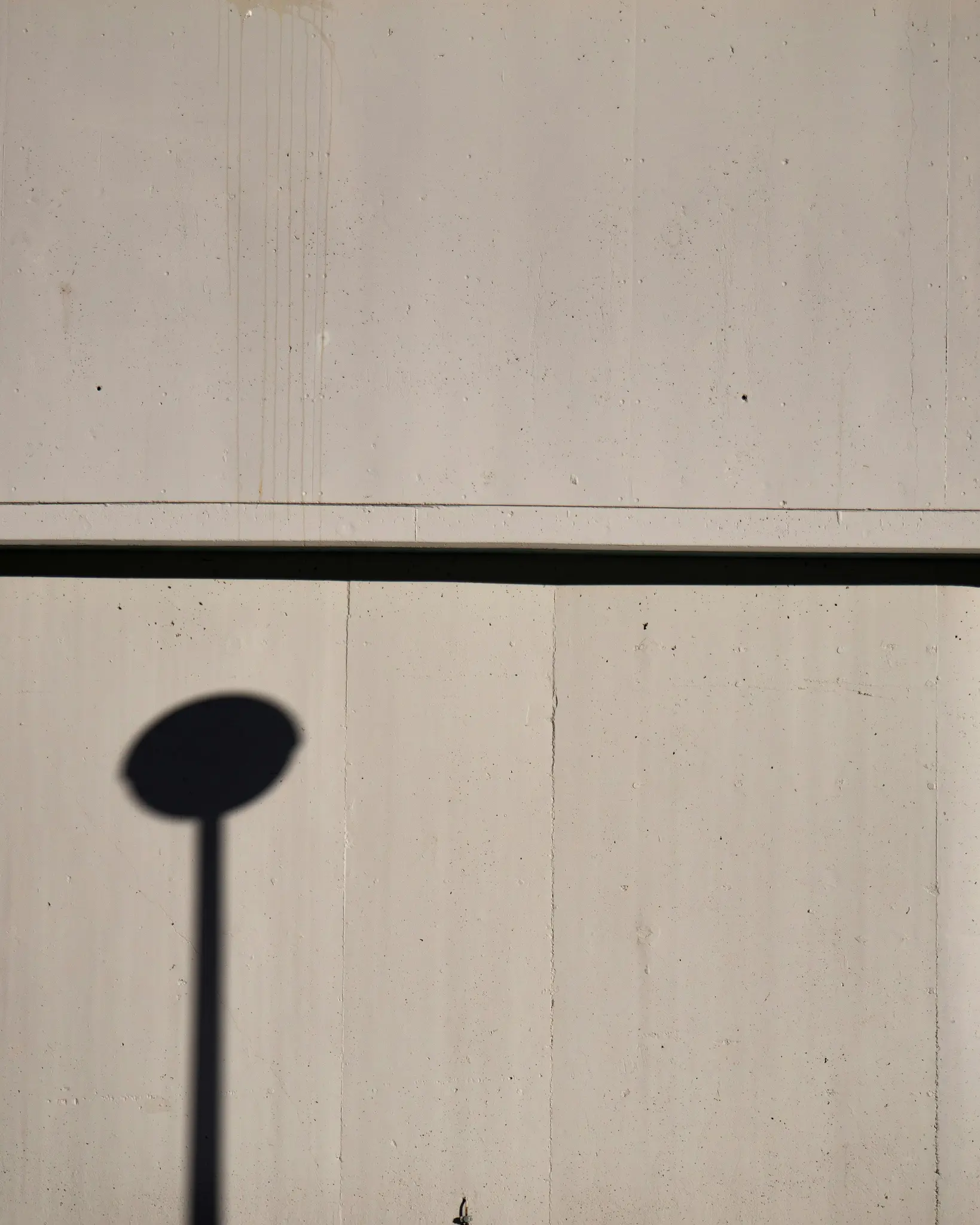 Una foto minimalista que muestra la sombra oscura de una farola con parte superior redonda y poste recto proyectada sobre un