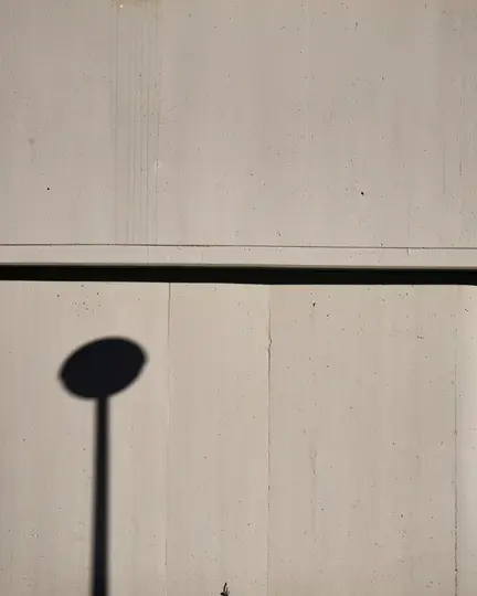Una foto minimalista que muestra la sombra oscura de una farola con parte superior redonda y poste recto proyectada sobre un