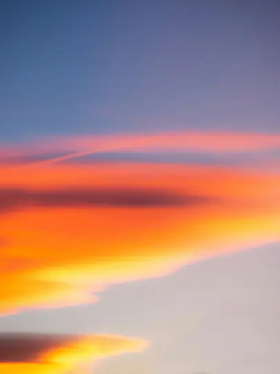 Uno scatto verticale di un cielo al tramonto, con bande di nuvole arancioni e gialle brillanti su uno sfondo sfumato di blu e