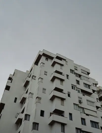 Una toma en ángulo bajo de un edificio alto y blanco con muchas ventanas y balcones, contra un cielo gris simple y nublado.