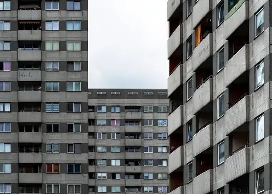 Un primo piano, ad altezza d'occhio, di tre edifici di appartamenti in cemento con molte finestre e balconi sotto un cielo