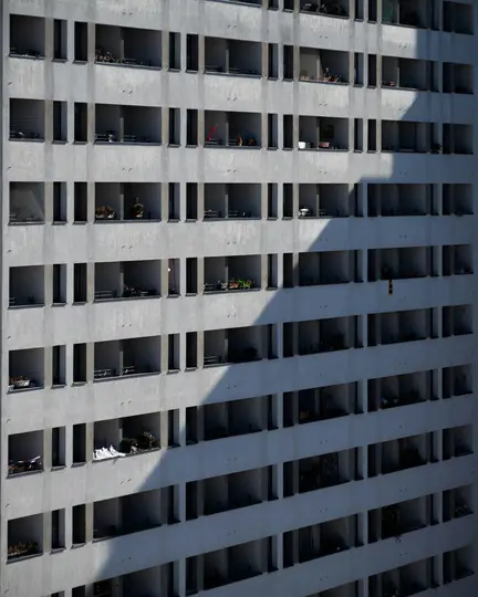 Una vista obliqua dall'alto della facciata di un moderno condominio. File di balconi rettangolari proiettano ombre diagonali.