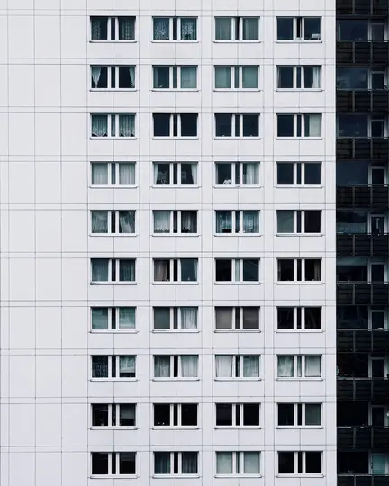 Una vista ravvicinata, frontale, della facciata di un edificio alto, con molte file di finestre rettangolari con cornici