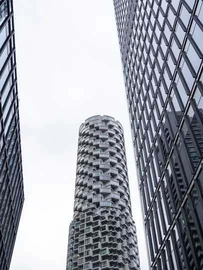 Una vista de tres rascacielos modernos desde un ángulo bajo. Un edificio cilíndrico con una fachada texturizada y angular