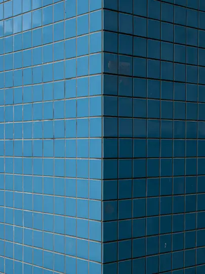 Una vista ravvicinata e astratta dell'angolo di un edificio coperto da piccole piastrelle quadrate blu con fughe grigie.