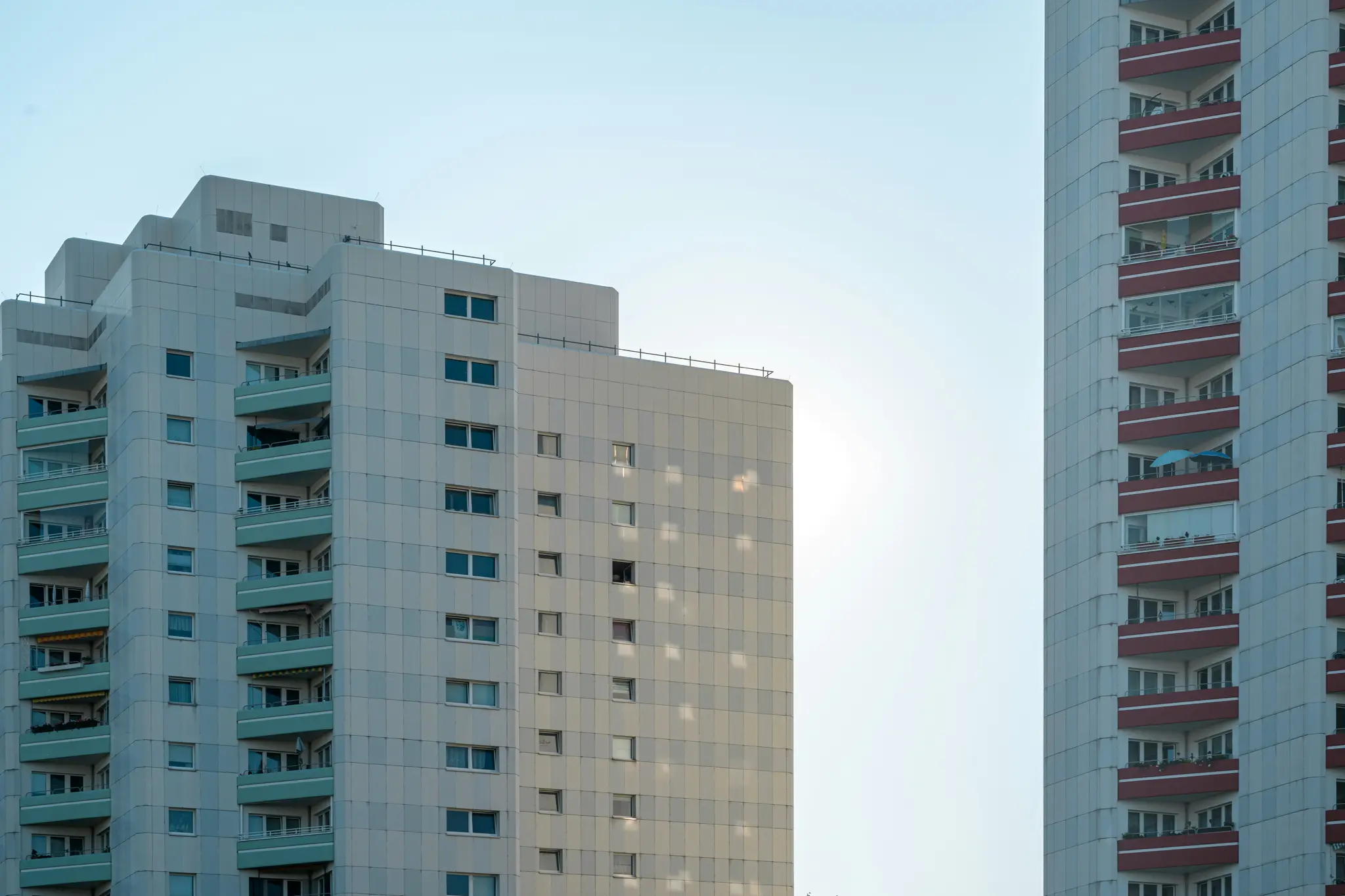 Dos edificios residenciales altos, uno con balcones de color turquesa y el otro con balcones rojos, se alzan contra un cielo