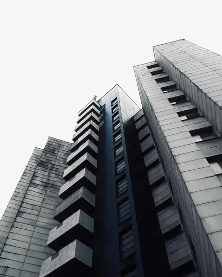 Una toma en ángulo bajo de tres edificios altos, grises y azul oscuro con balcones y ventanas geométricos, contra un blanco
