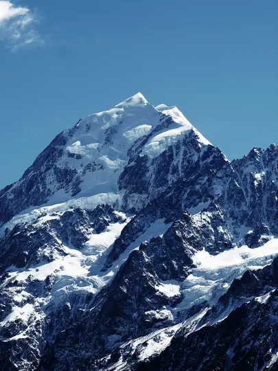 Un majestuoso pico de montaña nevado se eleva bruscamente contra un cielo azul claro y profundo. Nieve blanca y hielo cubren