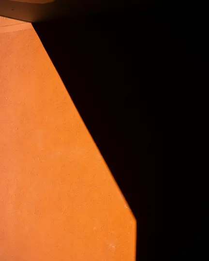O imagine abstractă, crudă a unui perete portocaliu texturat, divizat brusc de o umbră diagonală, creând un contrast