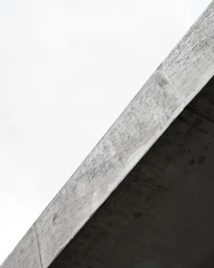 Una foto minimalista e astratta che mostra una trave di cemento diagonale con una superficie testurizzata su un cielo bianco