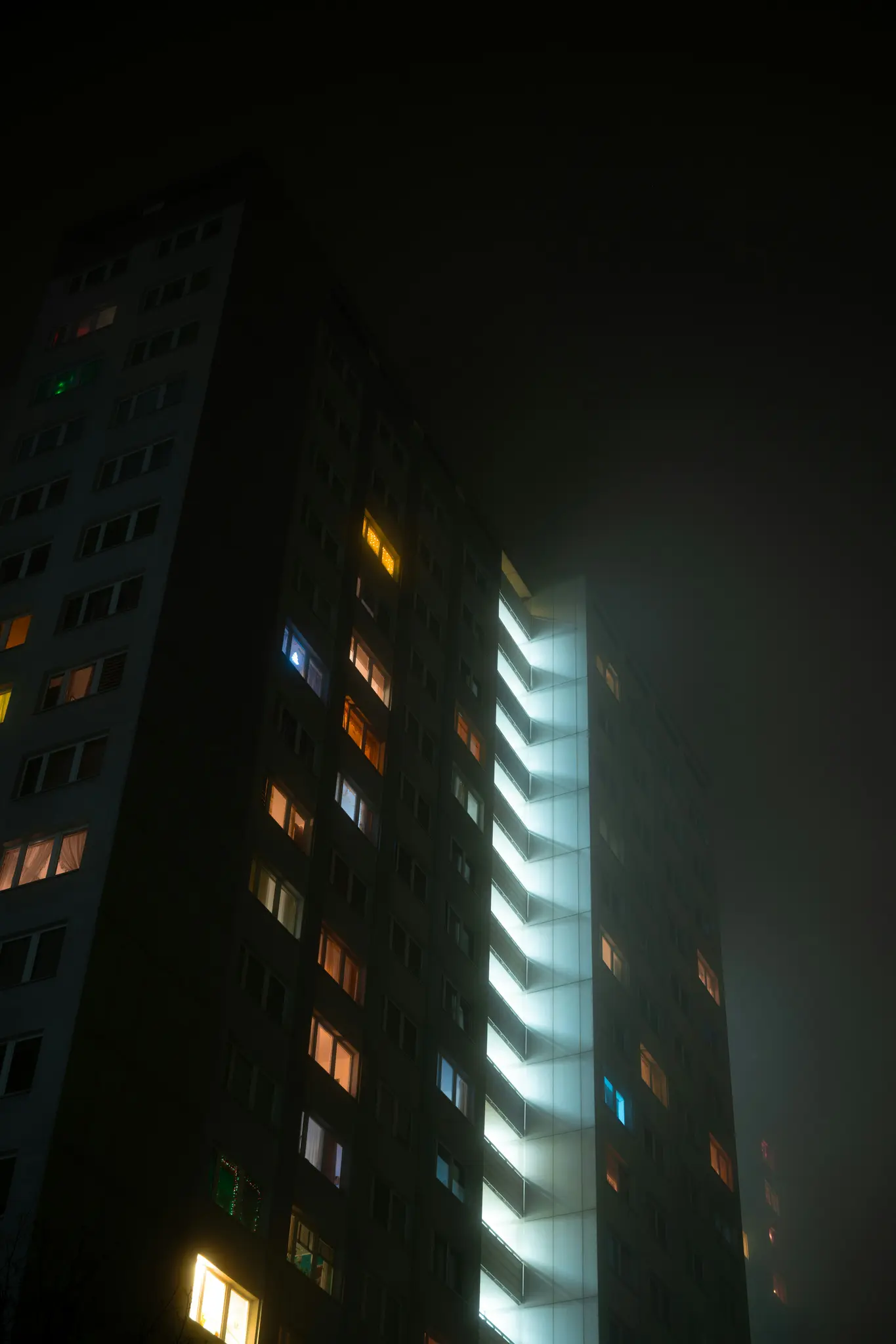 Una toma de ángulo bajo de un edificio alto y oscuro por la noche, con numerosas ventanas que brillan en varios colores