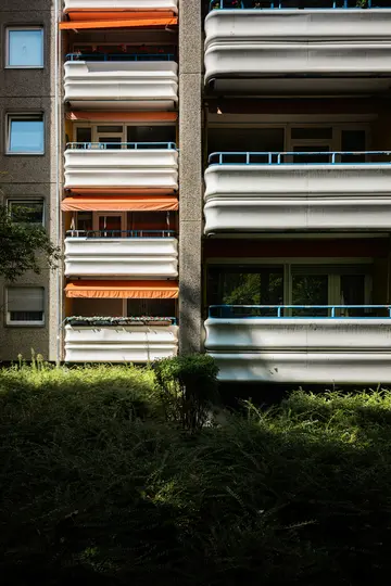 Una vista dettagliata della facciata in cemento di un condominio, con balconi bianchi con ringhiere blu e arancioni...