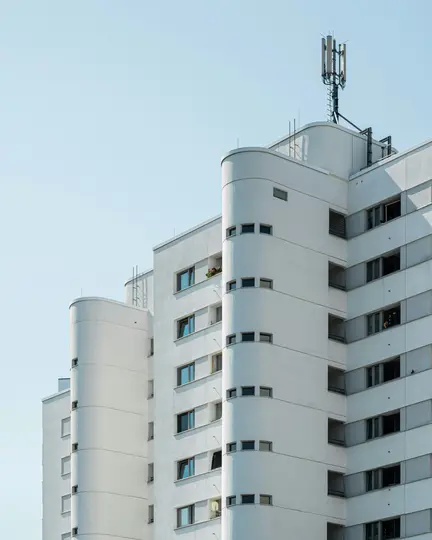 Un edificio bianco moderno e alto con angoli arrotondati e numerose finestre, sormontato da un'antenna cellulare, su uno