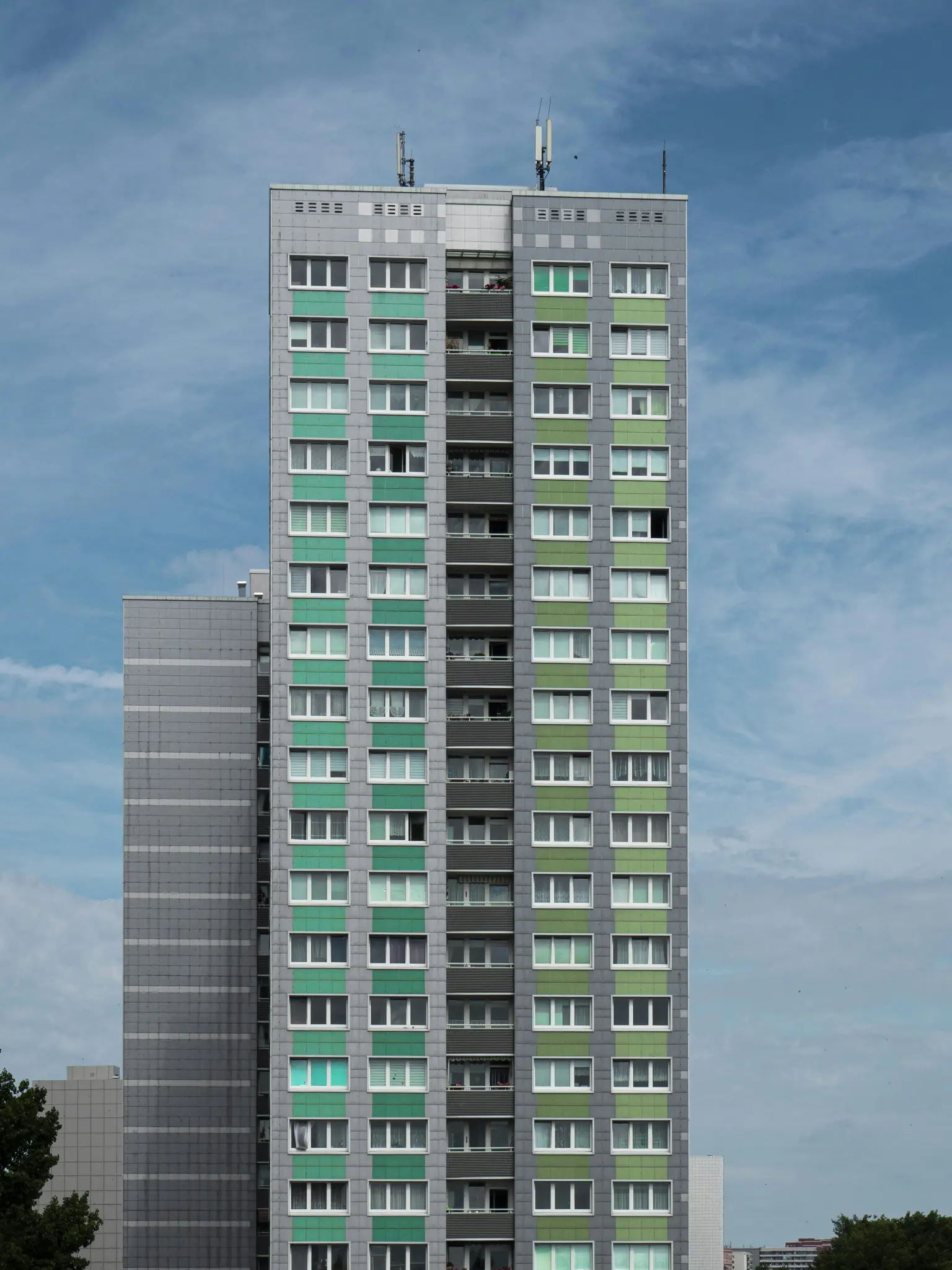 Un edificio residencial alto y moderno con paneles grises y verdes alternados y numerosas ventanas con marcos blancos bajo…