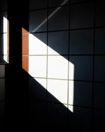 Una foto abstracta de alto contraste de una pared alicatada con patrones geométricos nítidos de luz solar y sombra profunda.