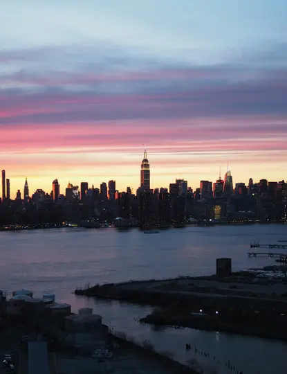 Un vibrante atardecer sobre el horizonte de una ciudad, con el Empire State Building prominente, visto a través de una masa