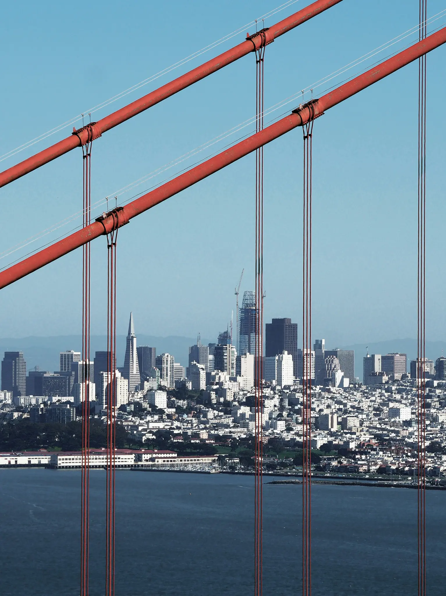 Pohľad na panorámu a záliv San Francisca, viditeľný cez červené diagonálne káble a zvislé závesné laná mosta Golden Gate.
