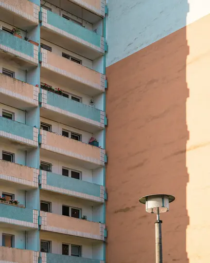 Μια κοντινή, κάθετη λήψη ενός κτιρίου διαμερισμάτων με ανοιχτόχρωμα μπλε και ροδακινί μπαλκόνια, δίπλα σε έναν απλό πορτοκαλί