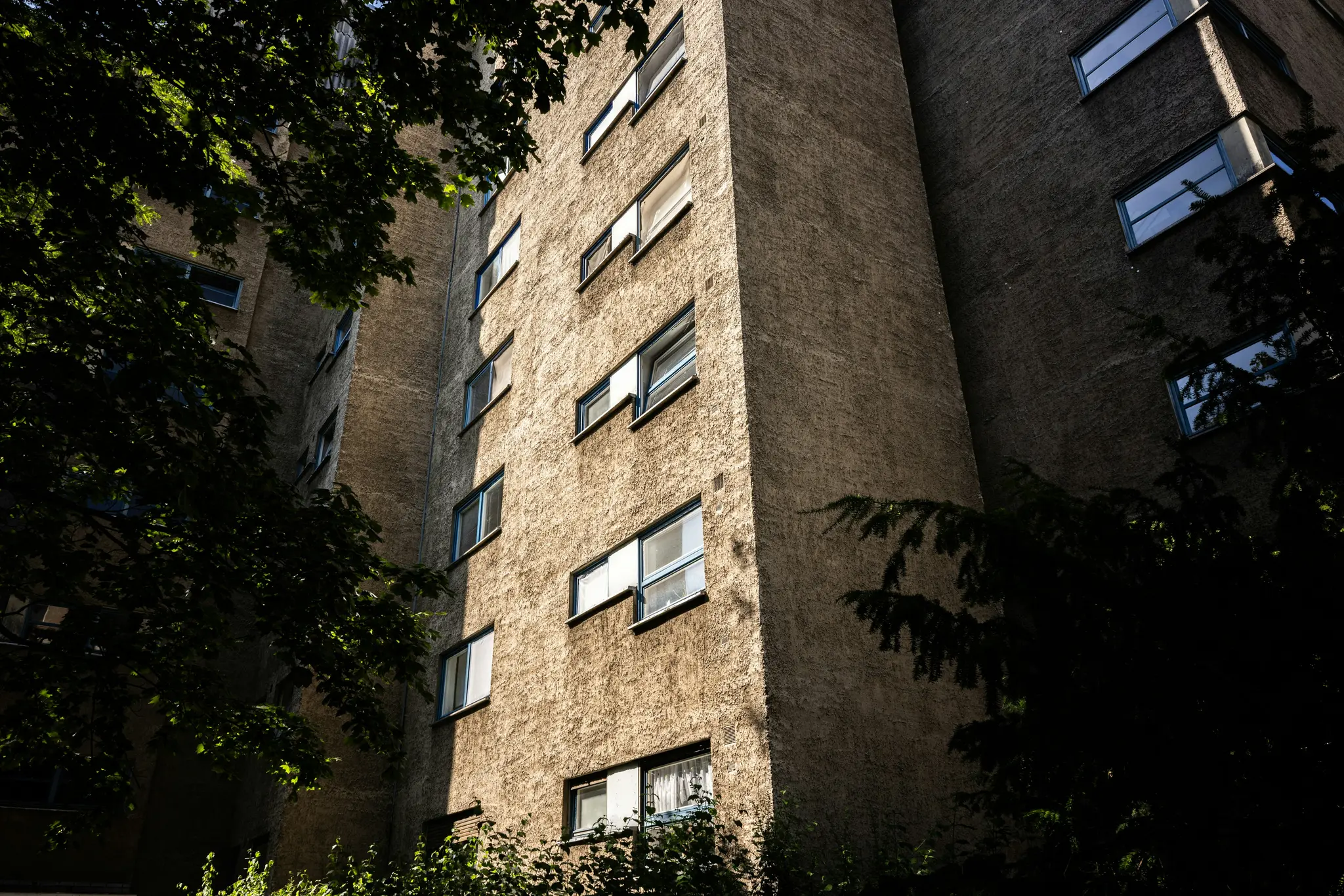 Una toma de ángulo bajo de un edificio alto y texturizado con muchas ventanas, parcialmente cubierto por hojas de árboles de