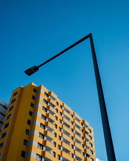 Una ripresa dal basso di un luminoso edificio giallo con accenti grigi e un lampione nero su uno sfondo di cielo azzurro