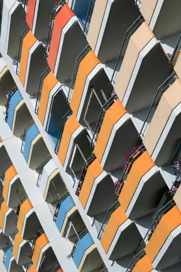 Una vista diagonale dal basso della facciata di un edificio moderno con molti balconi nei toni dell'arancione, rosso, blu e