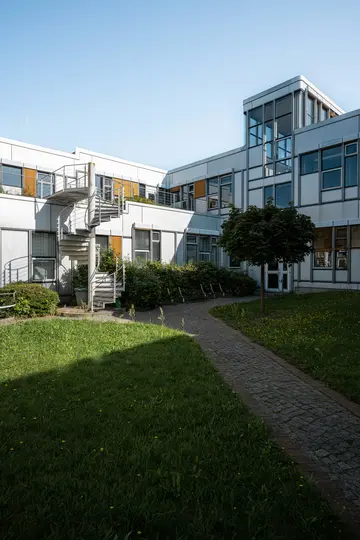 Moderni rakennus, jonka julkisivut ovat valkoiset ja harmaat, siinä on paljon ikkunoita ja vihreällä sisäpihalla on näyttävä
