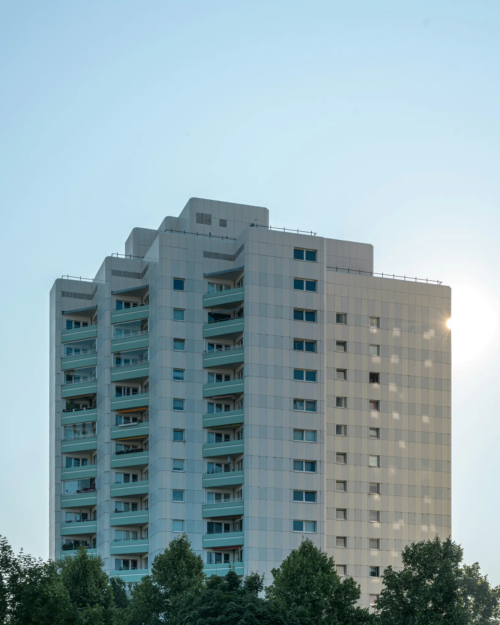 Un edificio de apartamentos alto y de color claro con una línea de techo escalonada y balcones de color verde azulado contra
