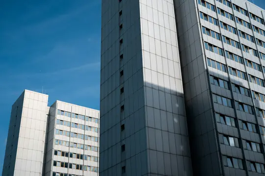 Una fotografia da un'angolazione bassa mostra tre moderni grattacieli con facciate grigie e bianche contro un cielo blu