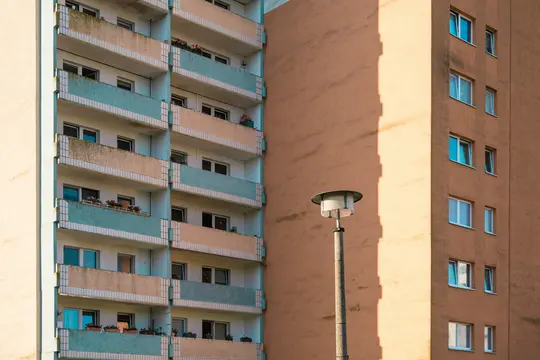 Un primo piano di due edifici. L'edificio a sinistra ha balconi con ringhiere blu chiaro e beige. L'edificio a destra ha…