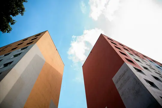 Uno scatto dal basso di due edifici alti e moderni con facciate nei toni dell'arancione, del rosso e del grigio, contro un